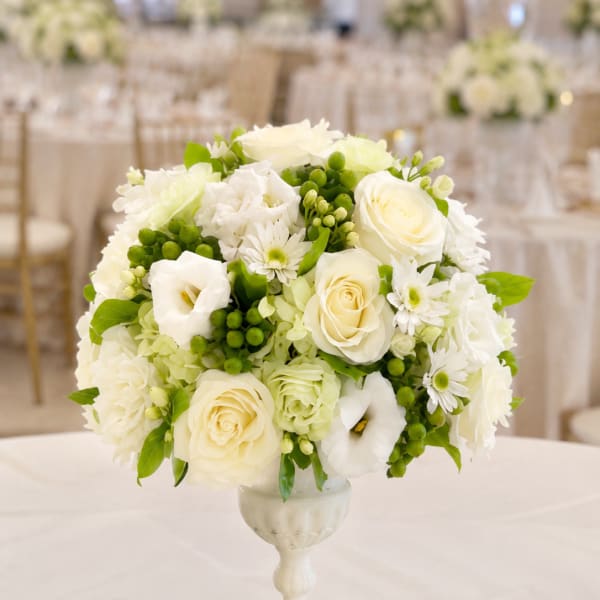 White floral arrangement in a pedestal vase with green accents