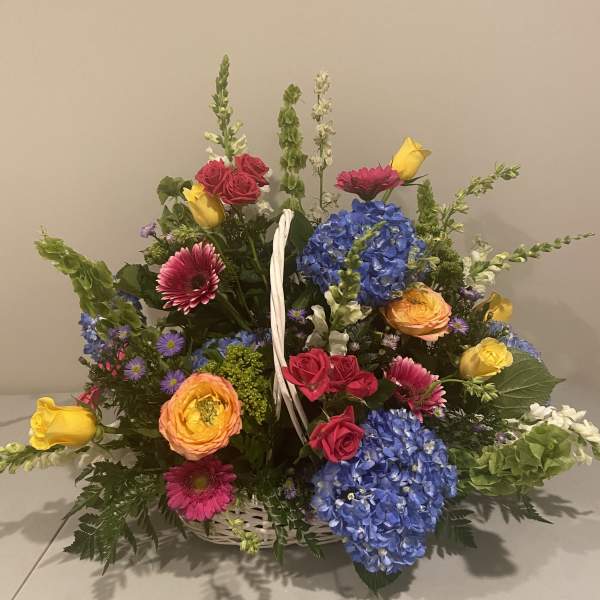 Basket arrangement with blue hydrangeas, roses, gerbera daisies, and yellow tulips