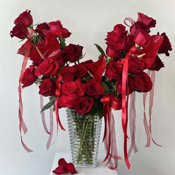 Red roses arranged in a clear ribbed vase with red ribbons