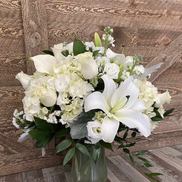 White floral arrangement with lilies, hydrangeas, and calla lilies in a glass vase