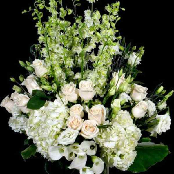White floral arrangement with roses, hydrangeas, and calla lilies in a glass vase