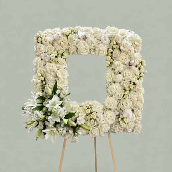 White floral wreath on a wooden easel with lilies and roses