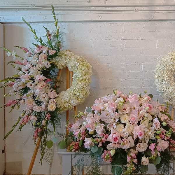 Three pastel floral wreaths and sprays on easels with a large pink centerpiece below.