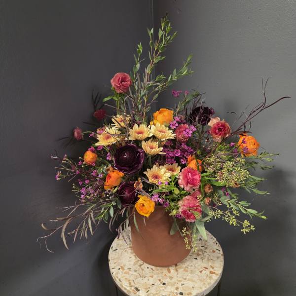 Mixed bouquet of orange, pink, and dark purple flowers in a terracotta vase