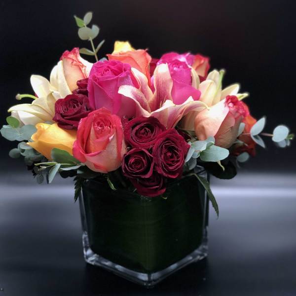 Bouquet of pink, red, and peach roses in a square glass vase