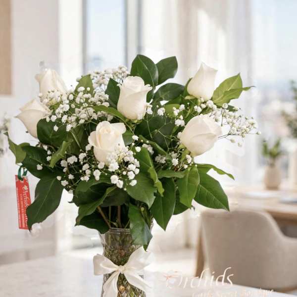 White roses and baby's breath in a clear glass vase with a ribbon