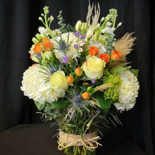 Mixed bouquet in a glass vase with white hydrangeas, roses, and orange spray roses