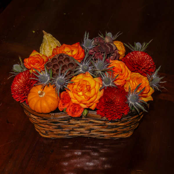 Basket arrangement with orange and red flowers, pumpkins, and thistle-like accents