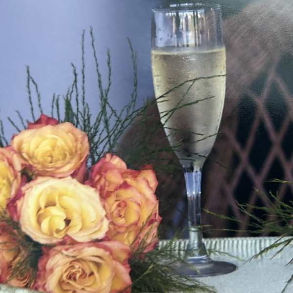 Yellow and pink roses arranged beside a champagne flute