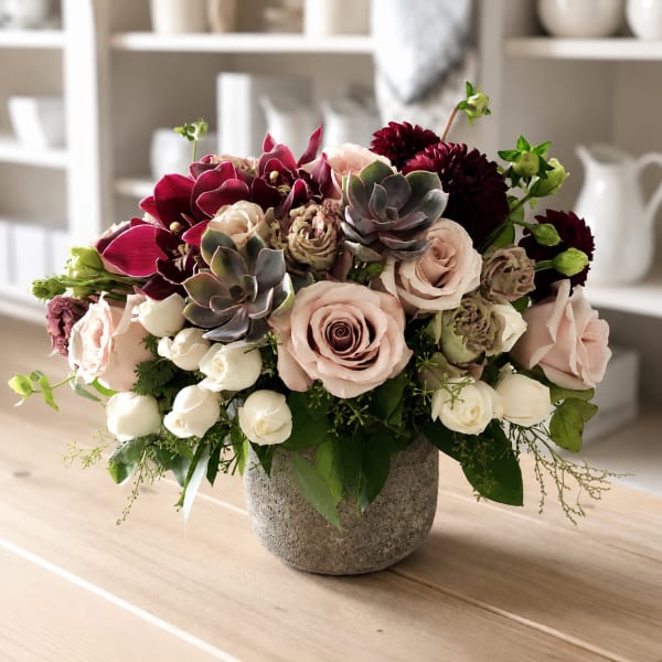 Mixed bouquet of blush roses, burgundy blooms, and succulents in a gray vase