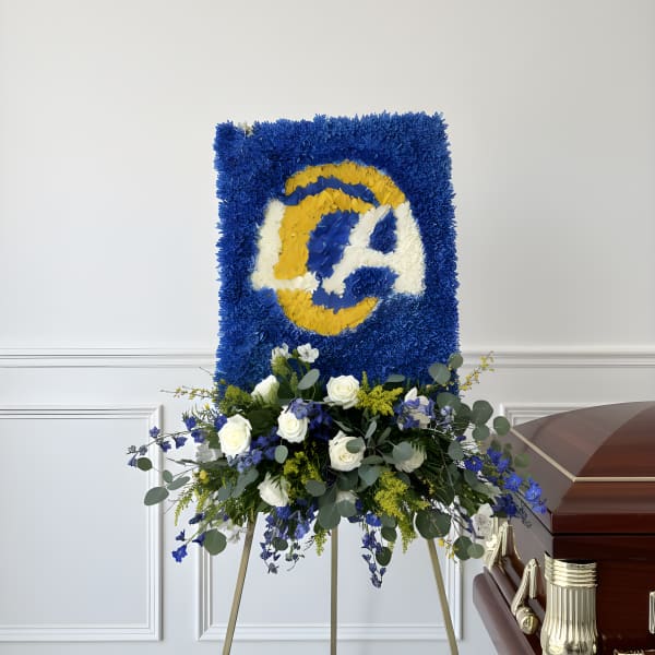Blue and yellow floral funeral tribute on an easel beside a casket