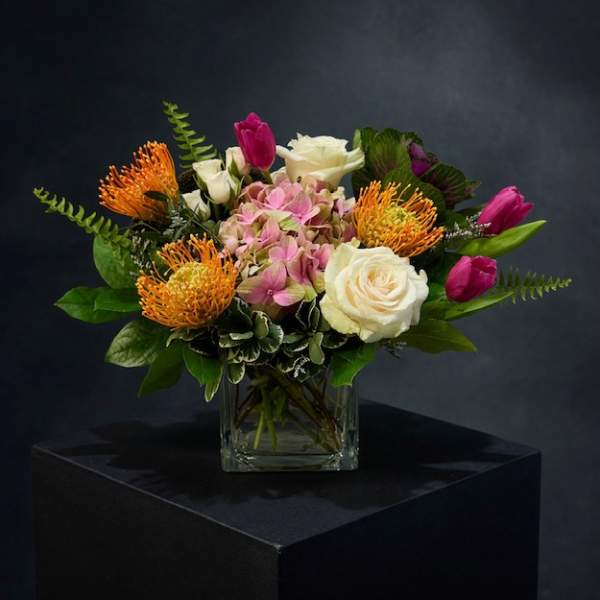 Mixed bouquet in a square glass vase with pink, white, and orange blooms