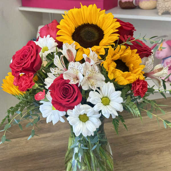 Bouquet of sunflowers, red roses, and white daisies in a glass vase