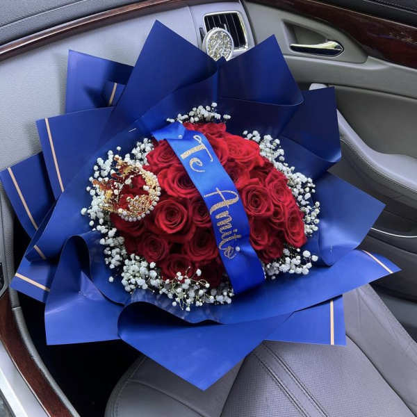 Red rose bouquet wrapped in blue paper with a crown topper