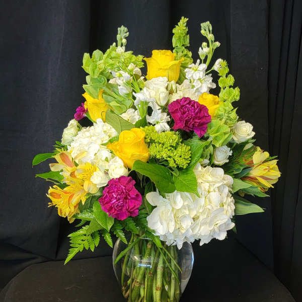 Mixed bouquet of yellow, white, and magenta flowers in a clear glass vase