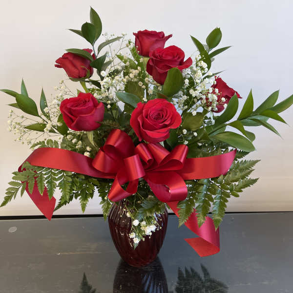 Red roses arranged in a vase with baby's breath and a red ribbon
