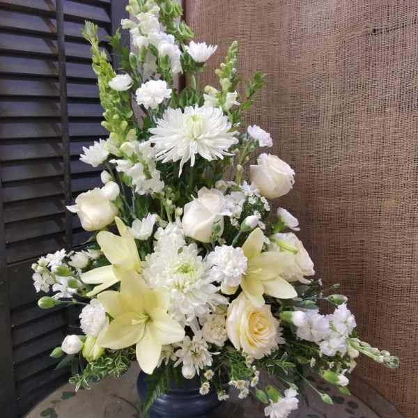 Tall white floral arrangement in a dark vase with lilies and roses