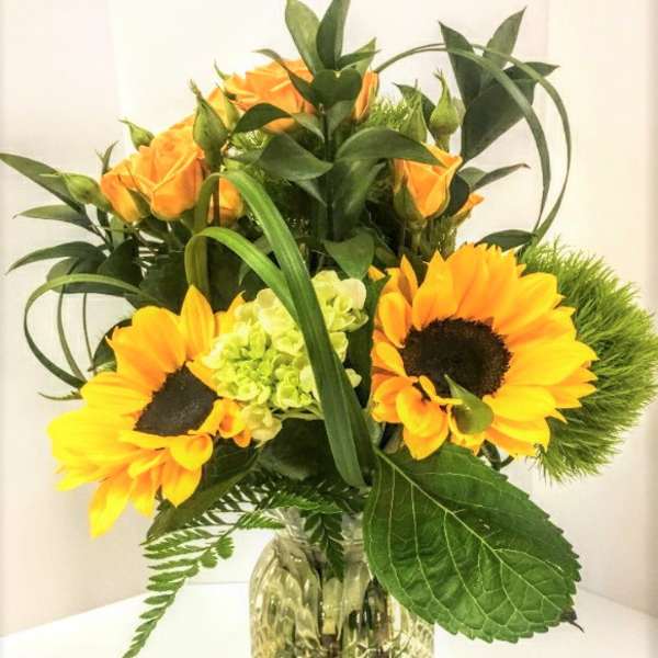 Sunflowers and orange roses arranged in a clear glass vase