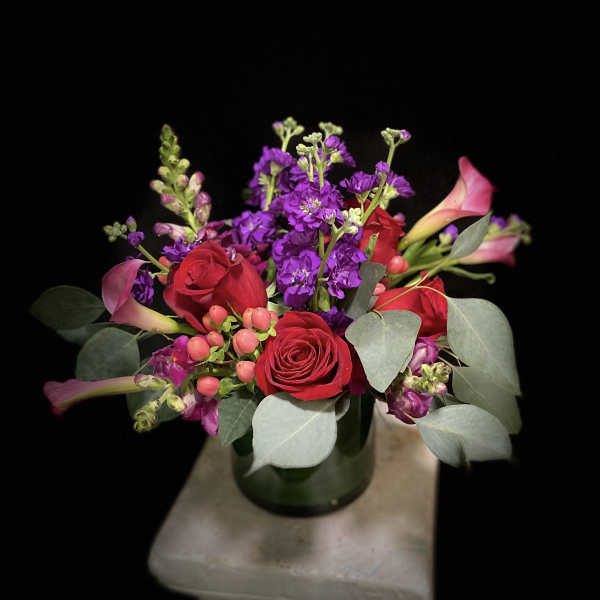Bouquet of red roses, purple flowers, and pink calla lilies in a glass vase