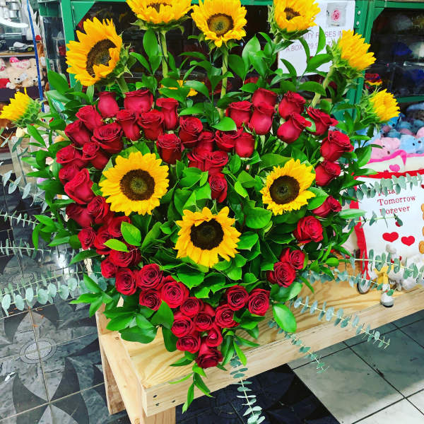 Heart-shaped bouquet of red roses and sunflowers on a wooden stand