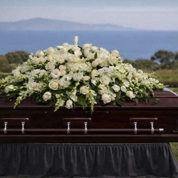 White floral casket spray on a dark wood coffin outdoors
