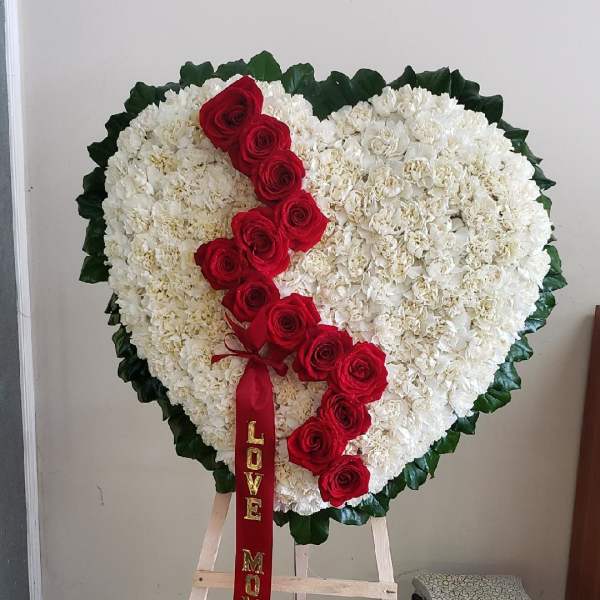 Heart-shaped floral tribute with white flowers and red roses on an easel