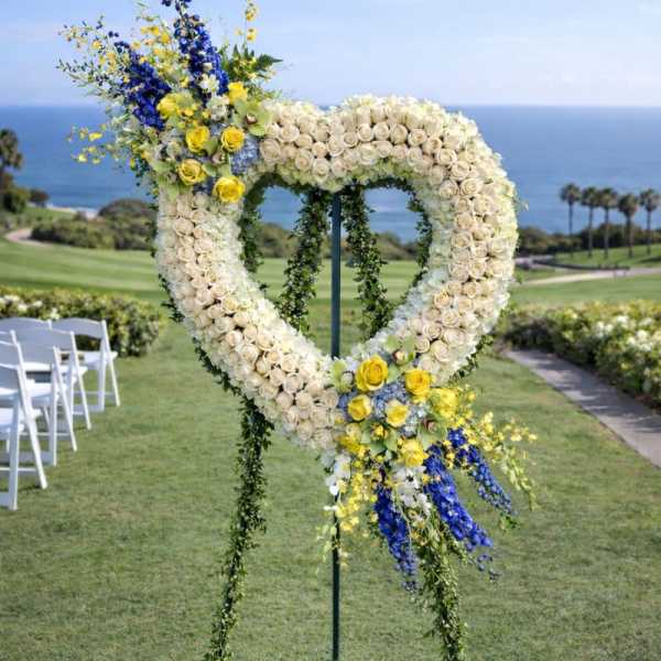 Heart-shaped floral wedding arch with white, yellow, and blue flowers