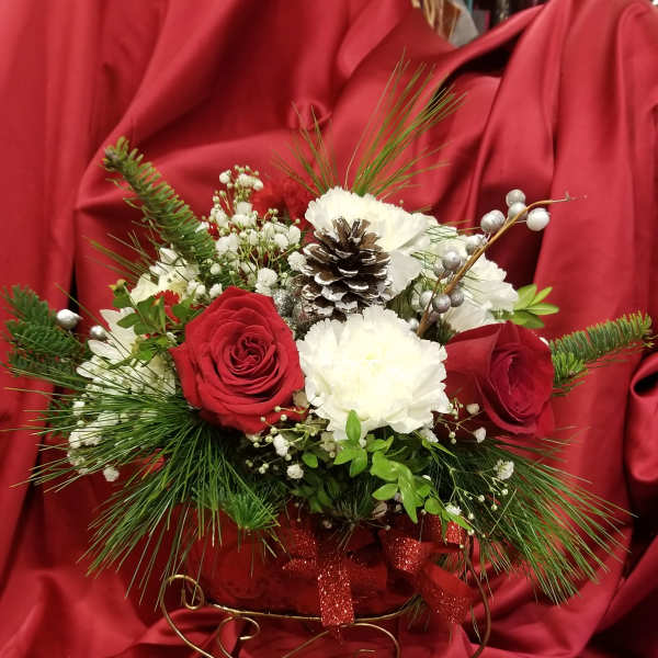 Red and white floral arrangement with pinecones and ribbon in a decorative holder