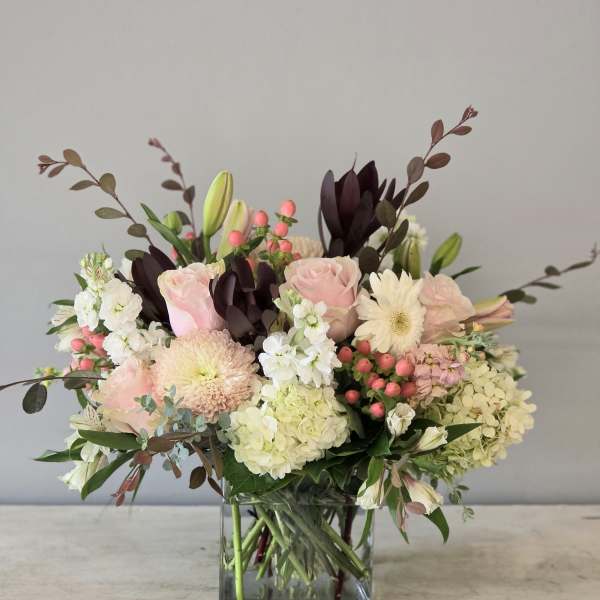 Pink roses and white blooms arranged in a square glass vase