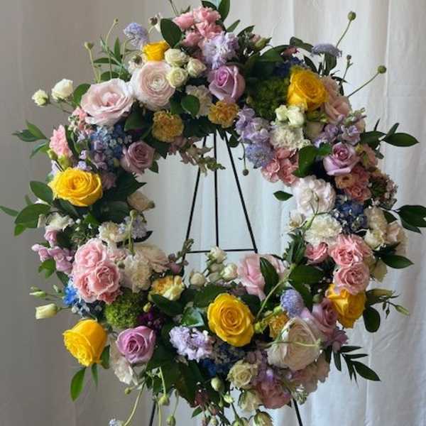 Large floral wreath on a black stand with pastel roses and mixed blooms