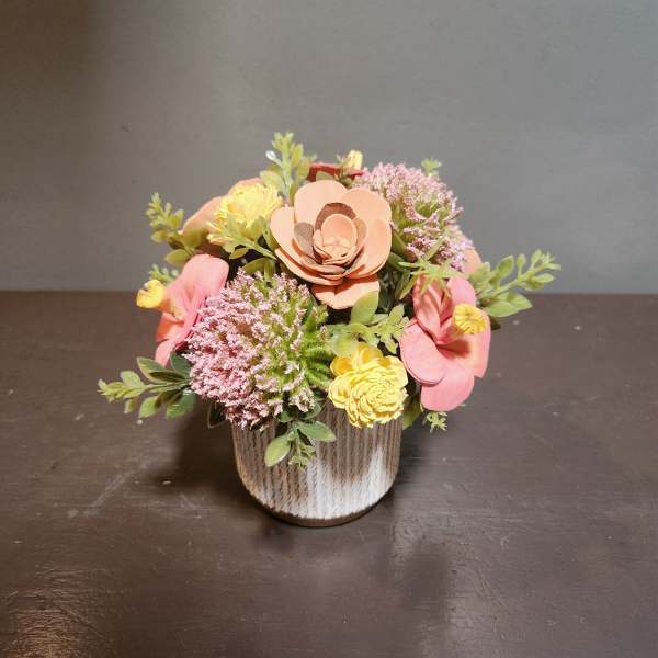 Small floral arrangement in a textured white pot with pink and yellow blooms