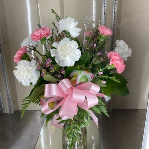Pink and white carnations in a glass vase with a pink ribbon