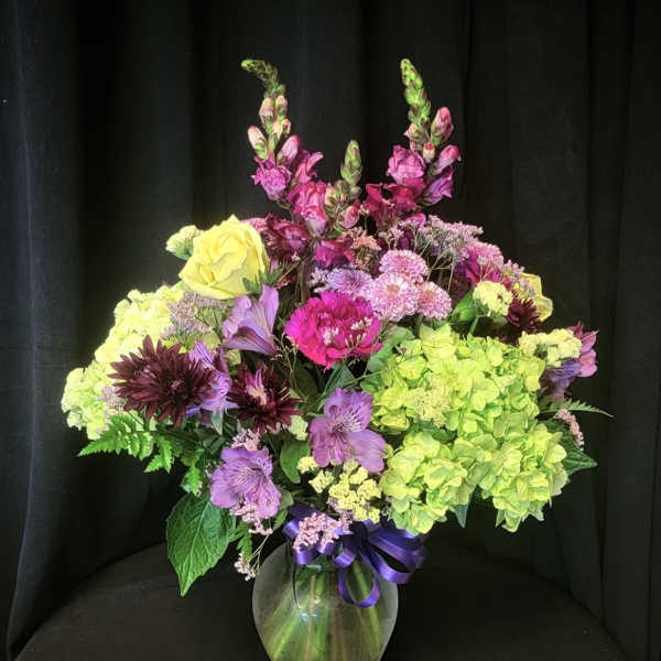 Mixed bouquet of purple, pink, and yellow flowers in a glass vase