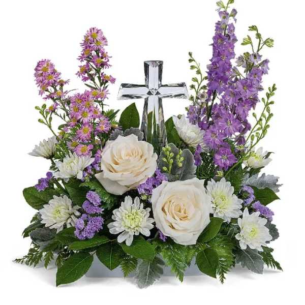White roses and purple flowers arranged around a clear glass cross