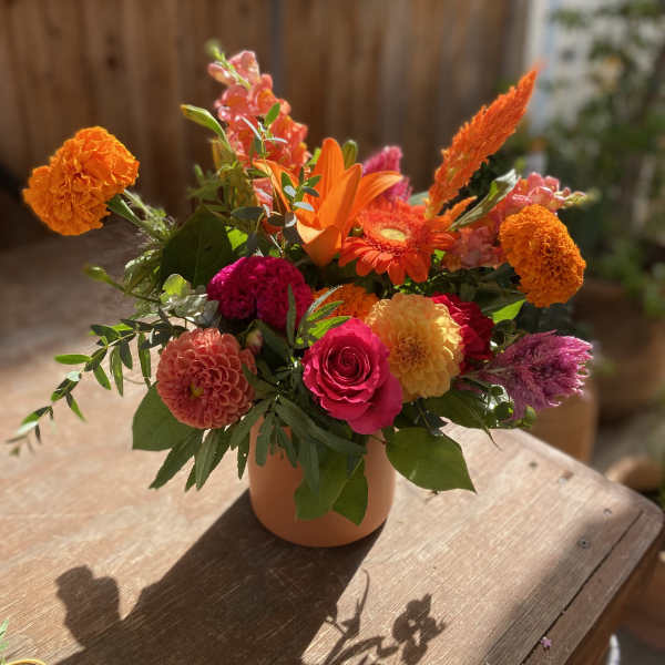 Bright mixed bouquet in a peach vase with orange, pink, and yellow blooms