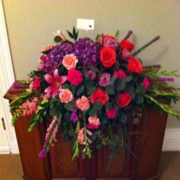 Large mixed floral arrangement with red roses and purple blooms in a wooden casket spray
