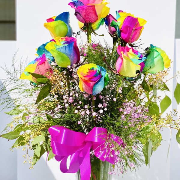 Rainbow-colored roses in a clear glass vase with a pink ribbon