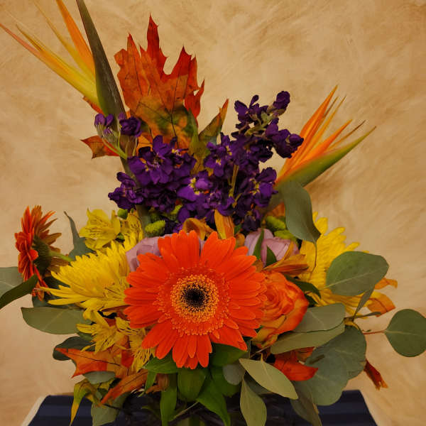 Bright mixed bouquet with orange gerbera daisies and purple flowers in a green vase
