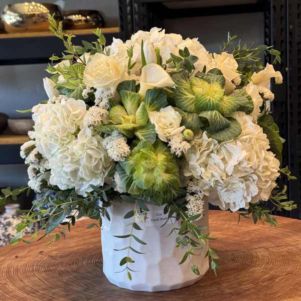 White floral arrangement in a white hatbox with trailing greenery