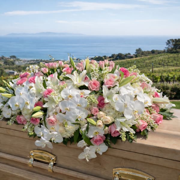 White and pink floral casket spray on a wooden casket