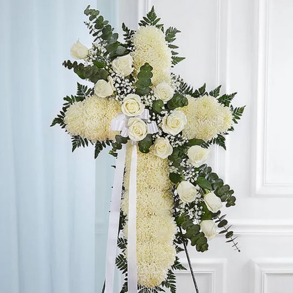 White floral cross arrangement with roses and ribbon on a stand