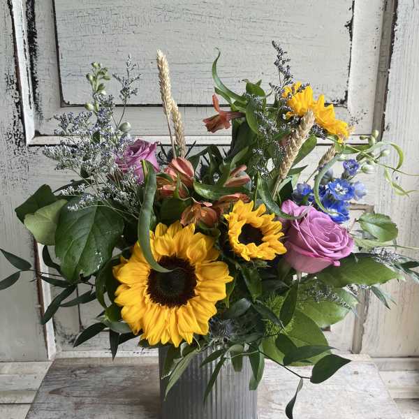 Mixed bouquet with sunflowers, pink roses, and blue flowers in a metal vase