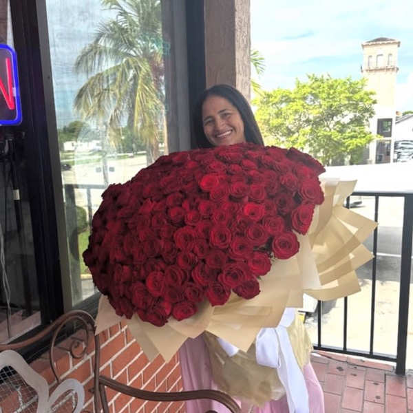 Woman holding a large bouquet of red roses wrapped in cream paper