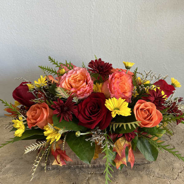 Arrangement of red and peach roses with yellow daisies in a low container
