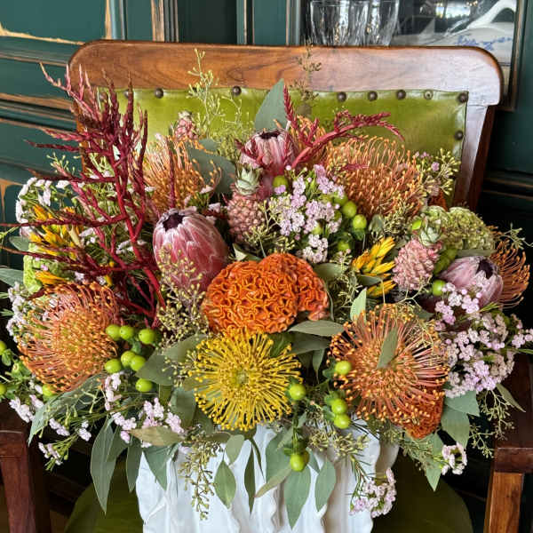 Mixed bouquet in a white ceramic vase with orange, yellow, pink, and green blooms