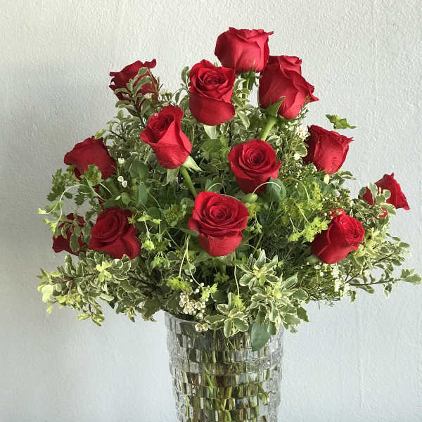 Red roses arranged in a tall glass vase with mixed greenery