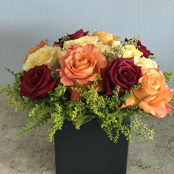 Mixed roses in orange, yellow, and red in a black square vase