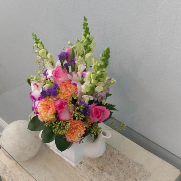 Pink and orange mixed flower arrangement in a white ceramic container