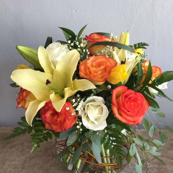 Bouquet of orange and white roses with yellow lilies in a woven basket