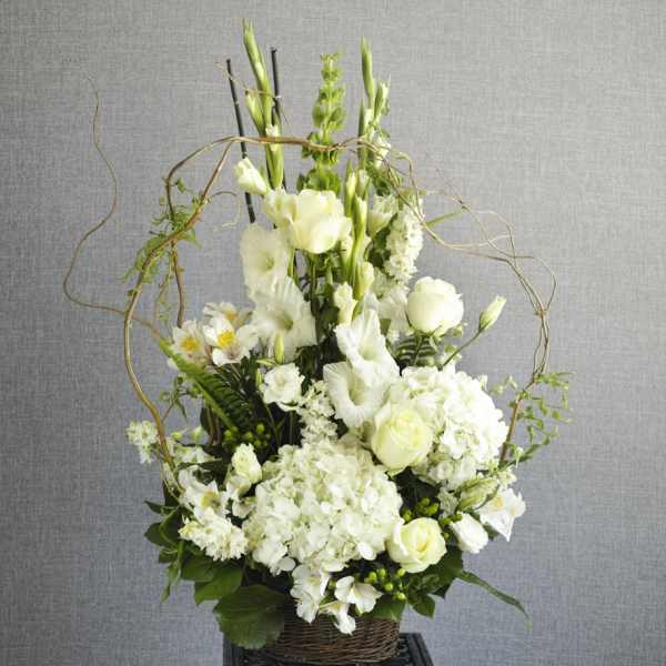 White floral arrangement in a wicker basket with tall stems and curly branches